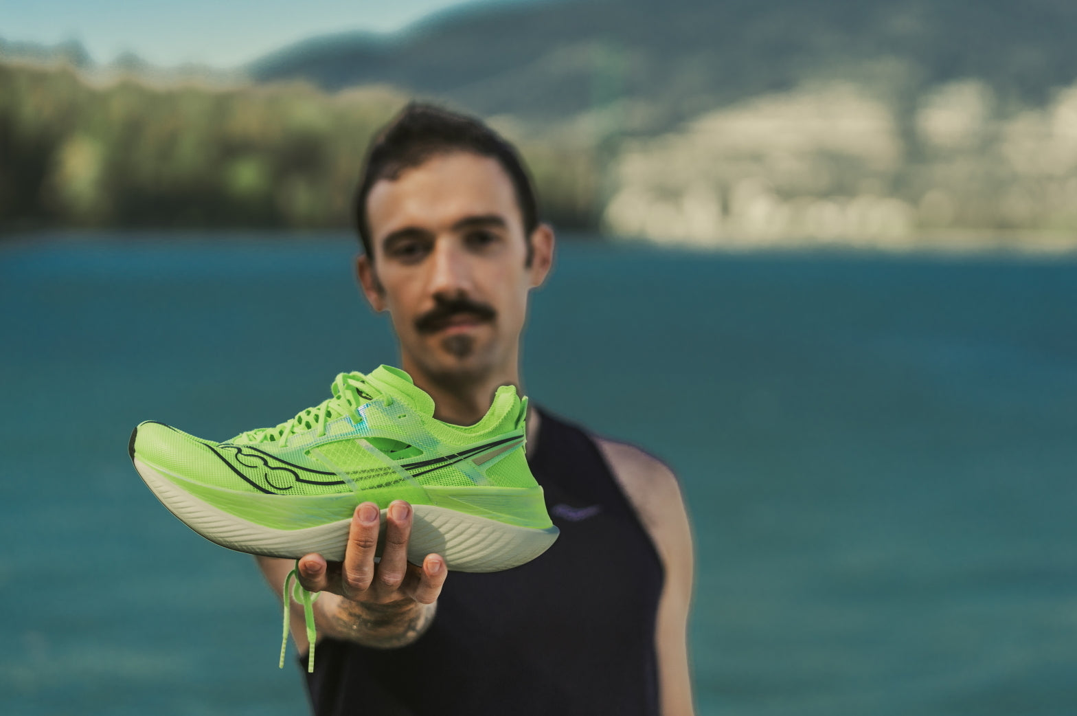 Ein Mann hält einen grünen Carbon-Laufschuh mit ausgestrecktem Arm in die Kamera